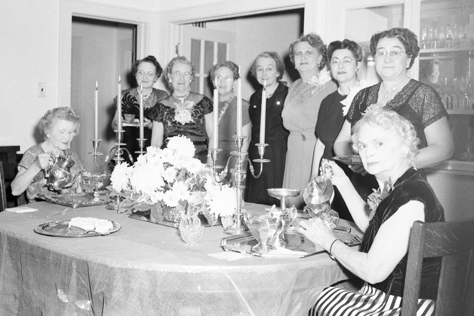 Ladies sitting and standing around dining room table.