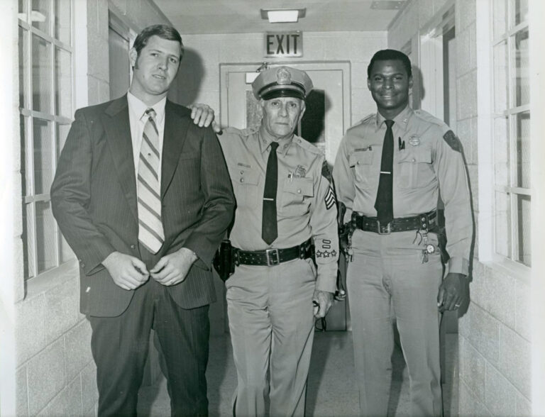 Officer Fletcher Ray, Arlington's first African American police officer, with Detective Larry Jones and Sergeant Harold White taken at 717 W. Main jail. Both Sergeant White and Officer Ray are in uniform and Detective Jones is in a suit.