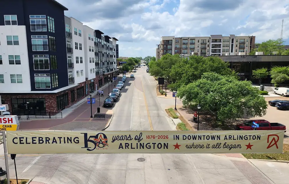 Beige banner stretched across Abram Street with text "Celebrating 150 Years of Arlington in Downtown Arlington Where It All Began 1876-2026."