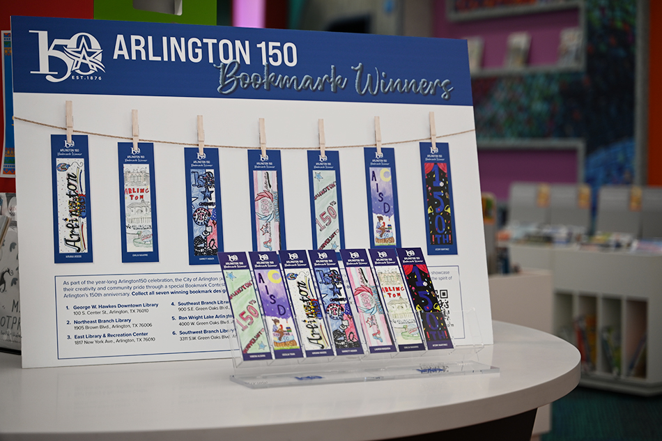 Seven bookmarks in holders with a poster behind them indicating which design is located at each Arlington Public Library branch.