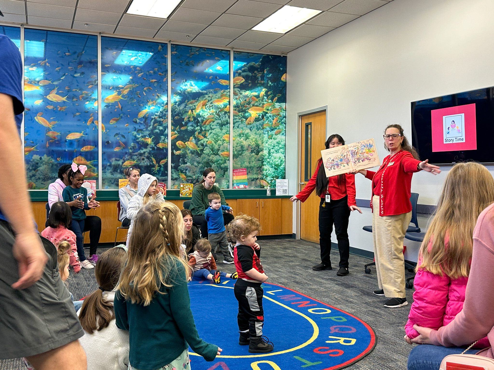 Librarians hold book and looks toward crowd during story time.