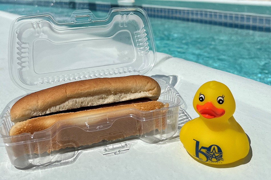 Hotdog and commemorative Arlington150 rubber duck placed on a ledge poolside.