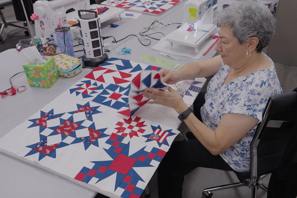 Woman placing pieces of a quilt together near sowing machine.