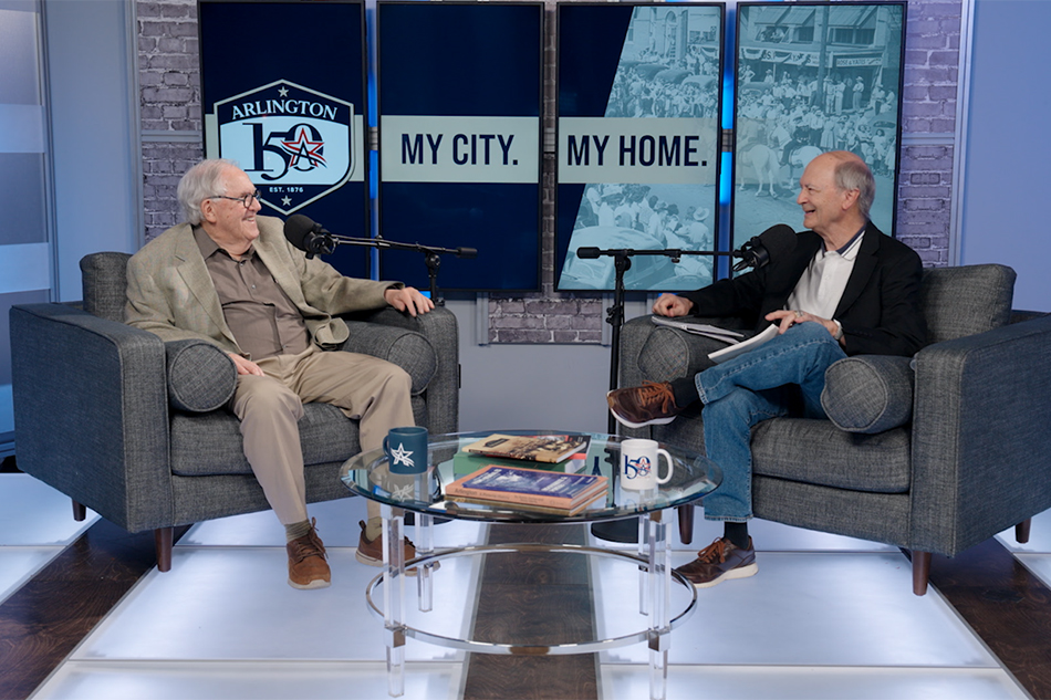 OK Carter and Jon Nelson sit in chairs behind microphones smiling at one another.