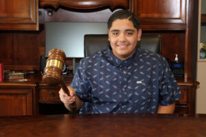 Honorary Mayor for the Day, Aaron Diaz, holds gavel and smiles for a photo.